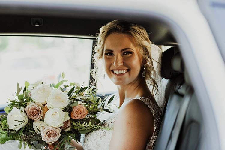Uśmiechnięta panna młoda z bukietem w samochodzie